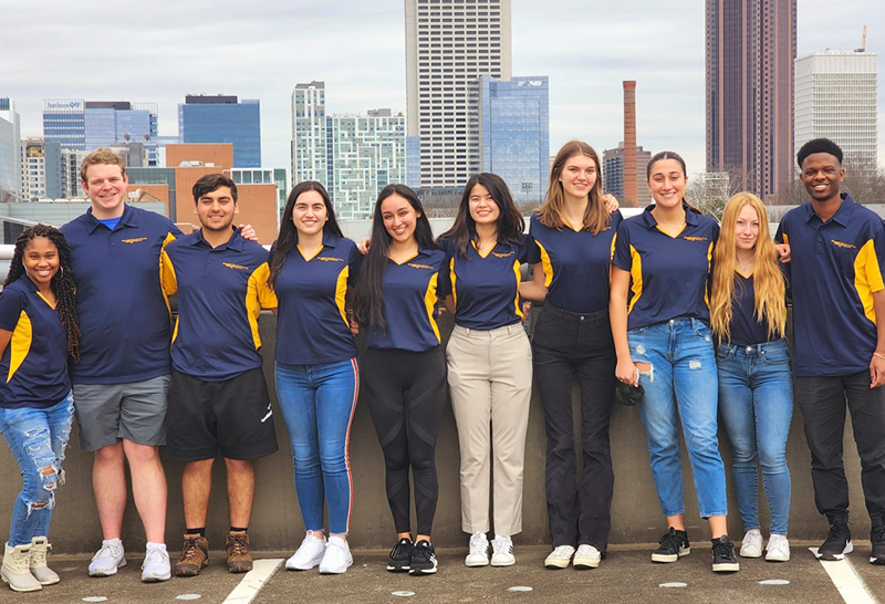 A group of young men and women (PALS) smiling to the camera with the ATL skyline as a backdrop.