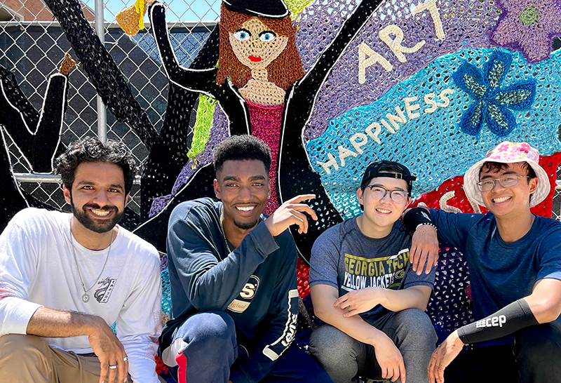 Four male GT students in front of a crochet mural that they worked on.